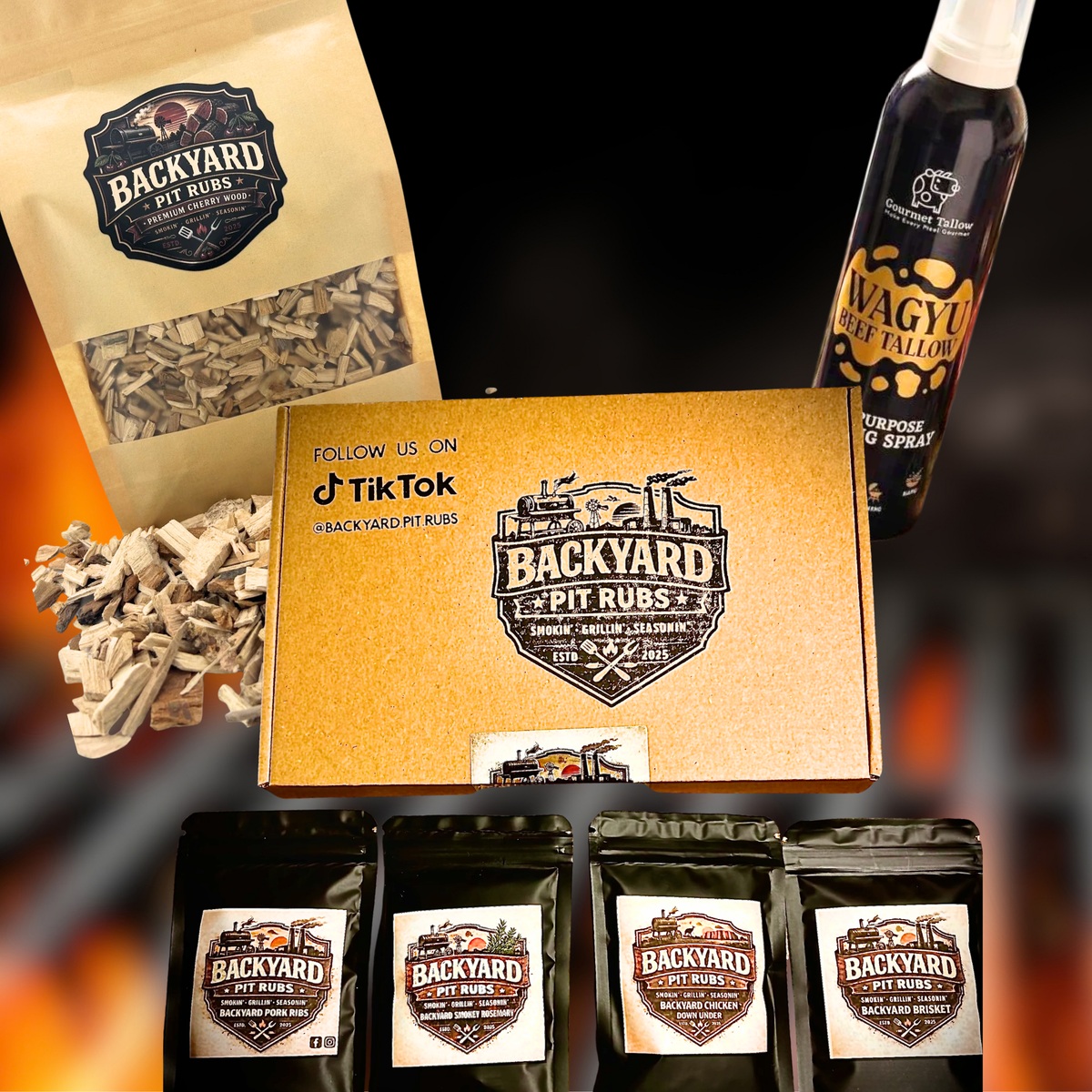 A Backyard Pit Rubs product bundle featuring a gold-coloured branded box, a kraft paper box of pit rubs, a bottle of wagyu fat lard oil, and four black pouches of rubs, arranged on a dark background with a blurred fire effect.